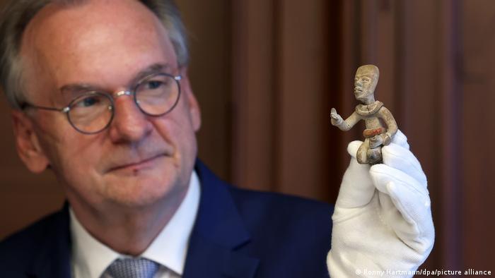 Saxony-Anhalt State Premier Reiner Haseloff holds a Mayan figure in his gloved hand 