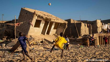 Children playing on beach with flood-damaged homes in the background on the coast of Senegal 