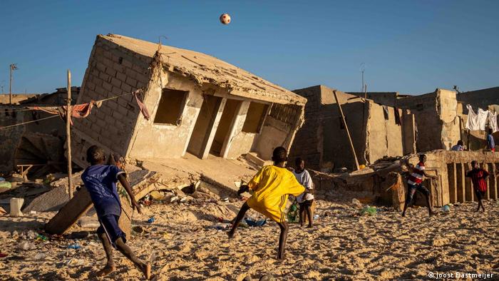 Niños jugando en la playa, al fondo casas destruidas por el agua en la costa de Senegal.