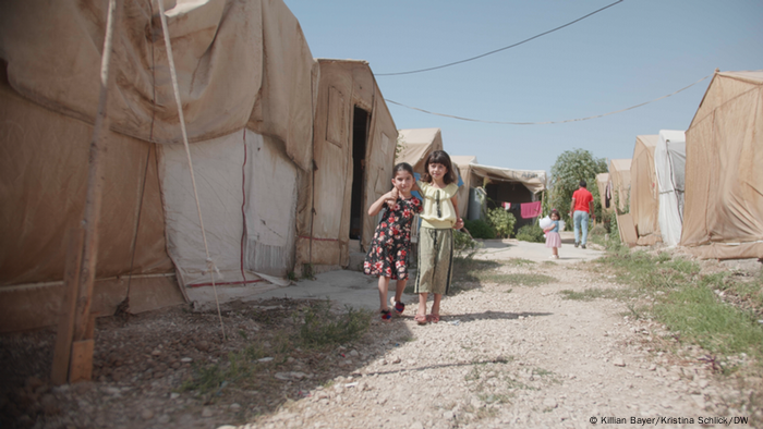 Two girls stand in a narrow lane between rows of beige tents