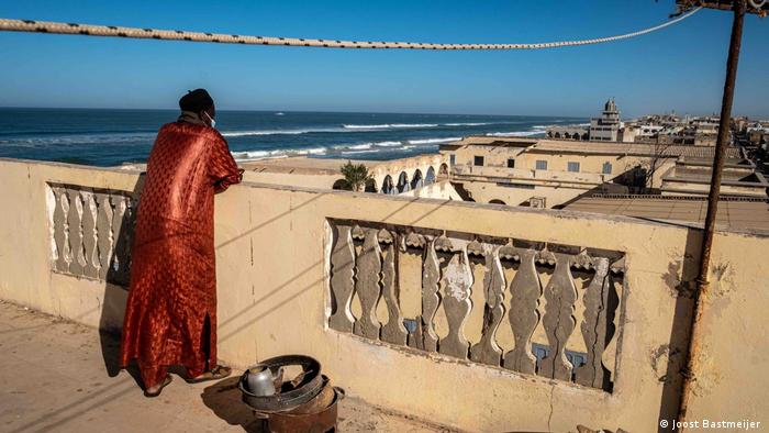 Ein Mann steht auf einem flachen Dach eines Stadthauses am Strand und blickt auf das Stadviertel am Meer Senegal Küstenerosion