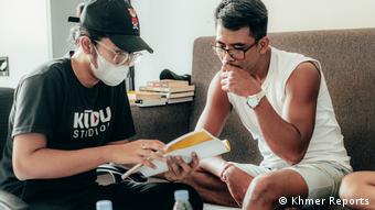 Khmer Reports director Kimseng Suon sits next to an actor with a script, briefing him on the action.