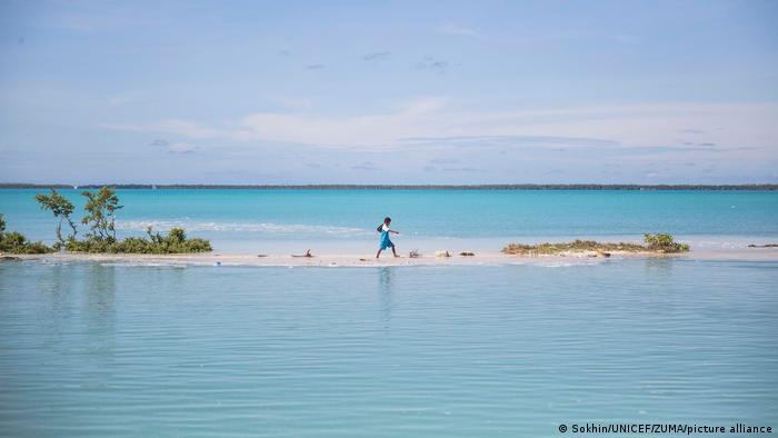 Un niño de camino a la escuela en Kiribati, sobre una superficie de arena, en medio del agua del océano.