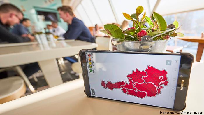 Ein Smartphone liegt auf einem Tisch in einem Lokal, es zeigt eine Landkarte von Österreich in der Farbe rot 