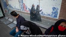 Iranian people sit at a bus-stand as two veiled schoolgirls walk past an anti-U.S. mural on a wall of the former U.S. embassy after a ceremony to mark the anniversary of the seizure of the U.S. embassy in downtown Tehran, November 4, 2021. (Photo by Morteza Nikoubazl/NurPhoto)