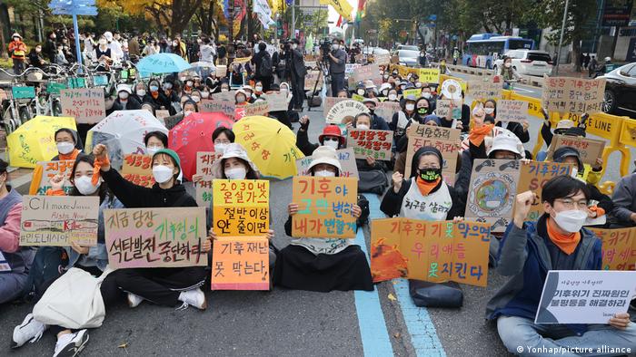 People sit in the street at an intersection in Seoul while holding signs demanding urgent action on climate change
