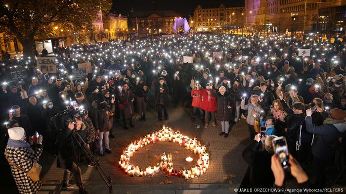 Protesters switch on the flashlight on their phones as they gather around candles organized in a heart-shape