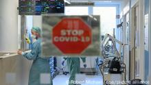 Intensivpfleger laufen in der Corona-Intensivstation des Universitätsklinikums Dresden über den Gang während im Vordergrund ein Schild mit der Aufschrift Stop Covid-19 an der Tür zu sehen ist.