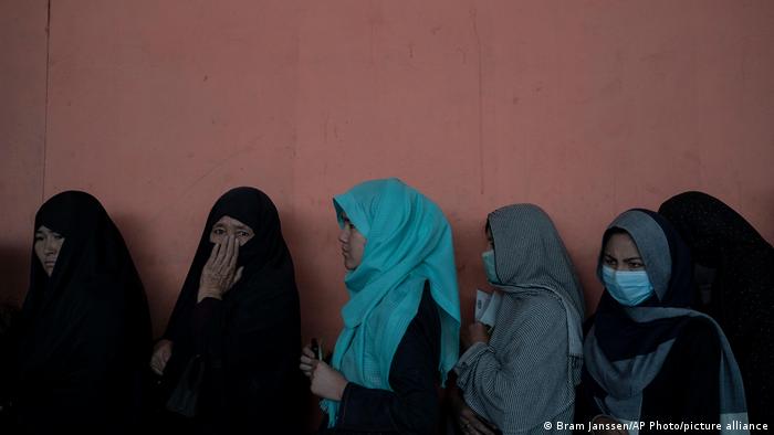 Women wait in a line to receive cash at a money distribution organized by the World Food Program (WFP) in Kabul