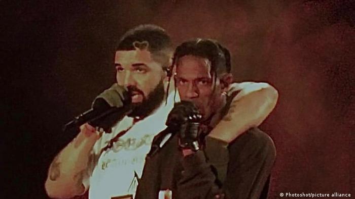 Rappers Drake has his arm around Travis Scott as they sing in microphones.