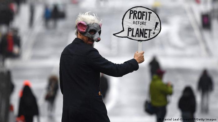 A demonstrator has an ironic placard saying that business puts profit before the planet