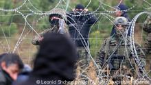 Polnische Grenzschutzbeamte stehen hinter einem Stacheldrahtzaun und bekämpfen Migranten, während sie sich an der weißrussisch-polnischen Grenze versammelt haben. Mehrere Hundert Migranten haben sich nach Angaben der Behörden in Belarus zu Fuß auf den Weg zur Grenze zum EU-Nachbarland Polen gemacht. +++ dpa-Bildfunk +++