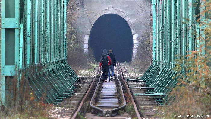 Two migrants walk across a railway bridge towards a tunnel at the border between Serbia and Kosovo