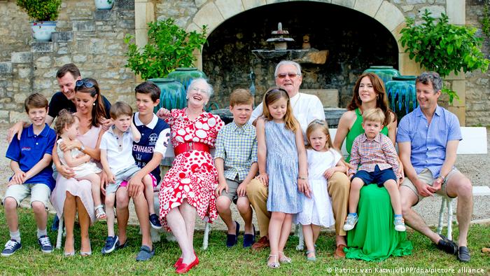 Königin Margrethe II. sitzt im Kreis ihrer großen Famile auf einer Bank 