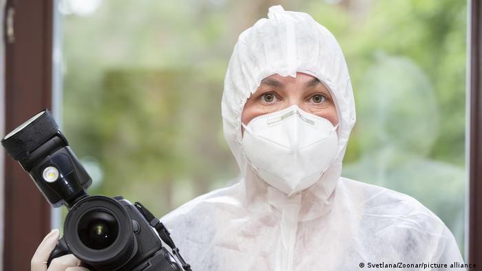 A woman in protective medical clothing holds a photo camera