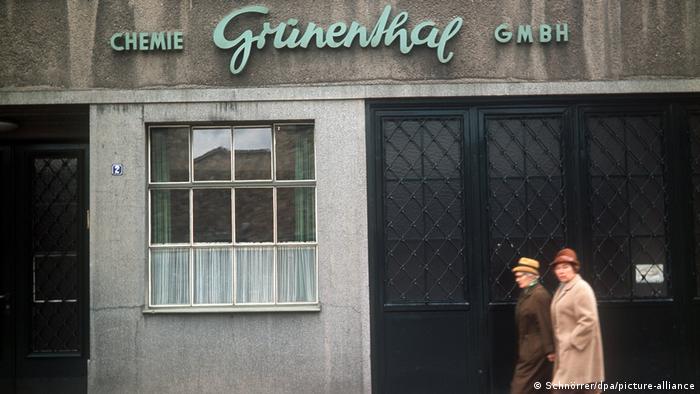 Zwei Frauen in Mantel und Hut laufen an einem Gebäude vorbei, auf dem zu lesen ist: Chemie Grünenthal GmbH