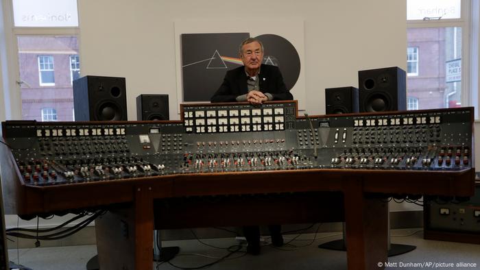 Pink Floyd drummer Nick Mason stands behind a large mixing console