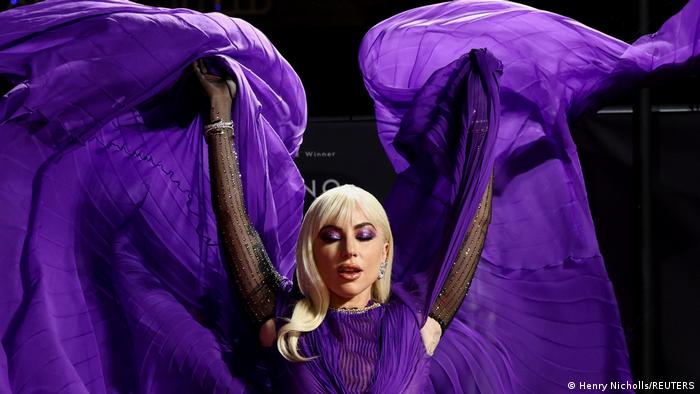 Lady Gaga pose avec une robe violette qu'elle soulève dans les airs, la faisant apparaître comme des ailes.