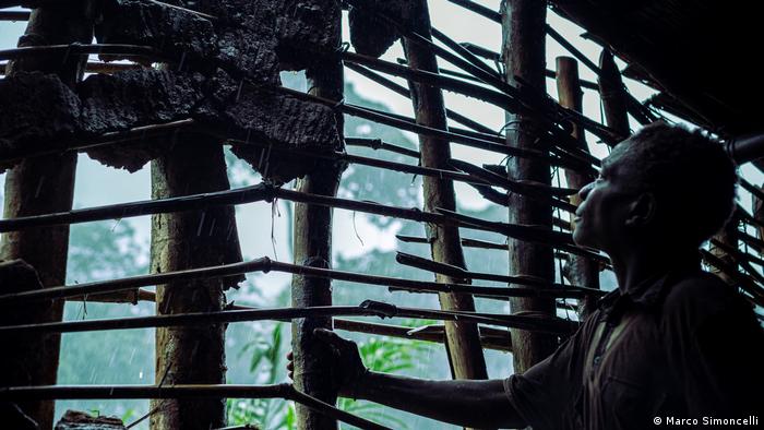 Un Pygmée regarde la forêt à travers les lattes d'une hutte.