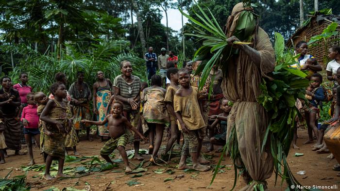 Un groupe de pygmées observe une personne déguisée en leur dieu de la forêt, Mobe.
