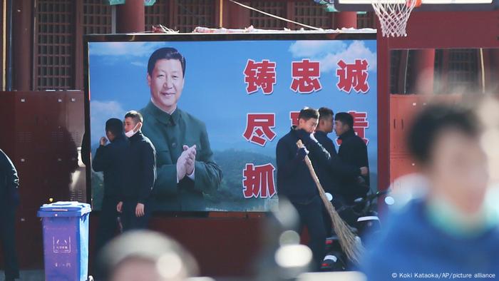 Pessoas caminham em calçada em frente a cartaz com a figura de Xi Jinping. O presidente de 68 anos assegurou sua permanência como líder da China para além de 2022