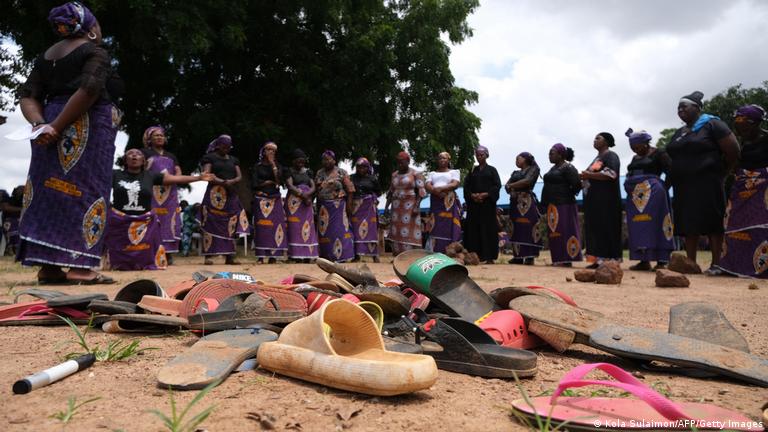 A group of women gather around abandoned shoes in a school yard.