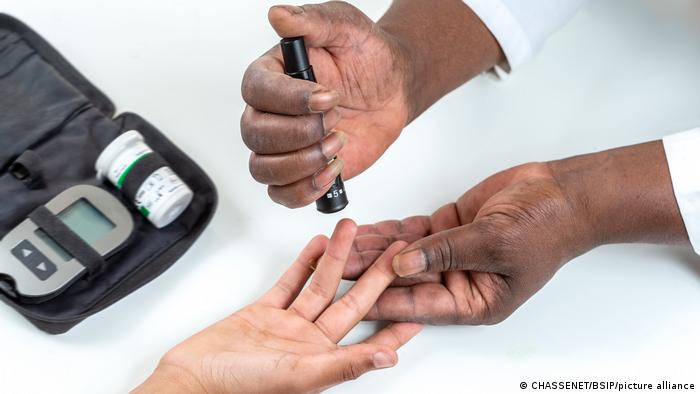 Close up photo of adult and younger hands holding a self-testing glucometer, which a diabeitc can use to check blood sugar levels at home.