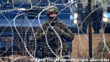 6693436 10.11.2021 A Polish serviceman stands guard behind a barbed wire near a migrant camp on the Belarusian-Polish border in Grodno region, Belarus. Migrants from the Middle East and North Africa trapped in Belarus have converged on the border with Poland, where razor wire fences and Polish troops have repeatedly blocked their entry. Viktor Tolochko / Sputnik