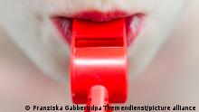 ILLUSTRATION - Eine Frau hält am 14.08.2014 in Berlin eine rote Trillerpfeife zwischen ihren Lippen. Foto: Franziska Gabbert