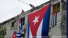 Men hang Cuban flags over the windows of opposition activist Yunior Garcia Aguilera's home in an attempt to stop him from communicating with the outside, as he holds a flower from a window, in Havana, Cuba, Sunday, Nov. 14, 2021. (AP Photo/Ramon Epinosa)