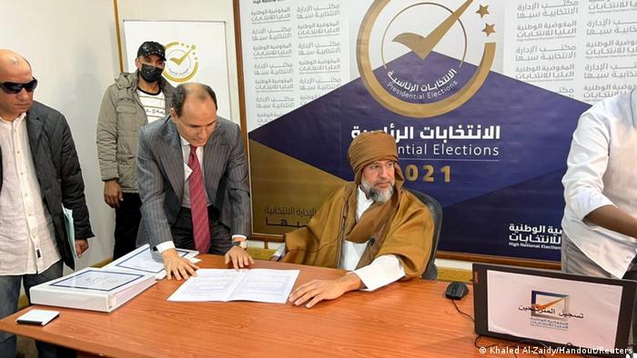 Seif al-Islam Gadhafi sits at a table to sign documents