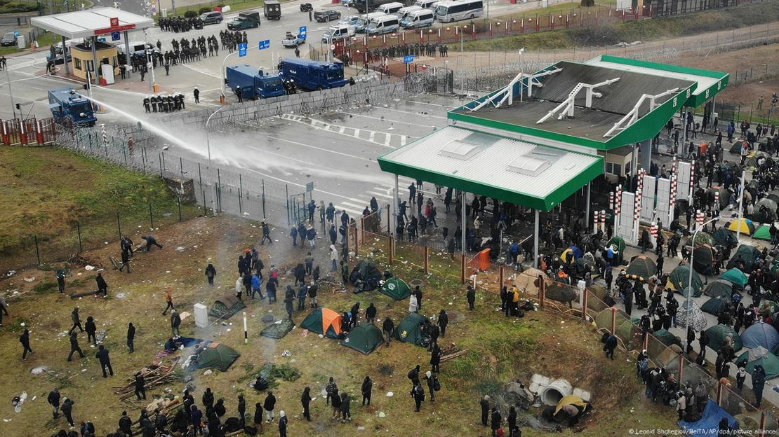 Imagem aérea de um posto de controle na fronteira entre Polônia e Belarus, com soldados poloneses de um lado e centenas de migrantes do outro