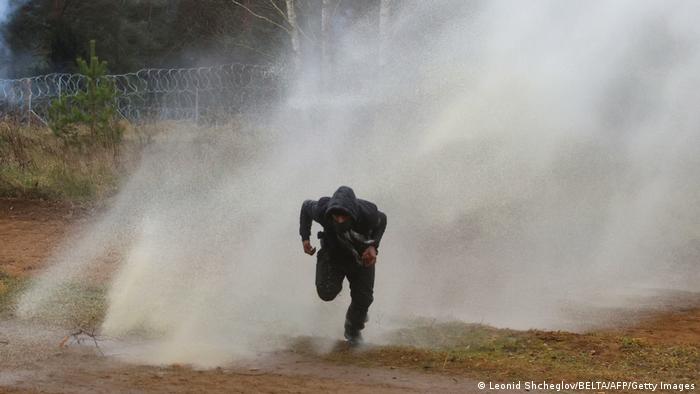 Un migrante huye de un cañón de agua en la frontera entre Polonia y Bielorrusia.