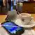 Taça de café, celular e máscara numa mesa de restaurante