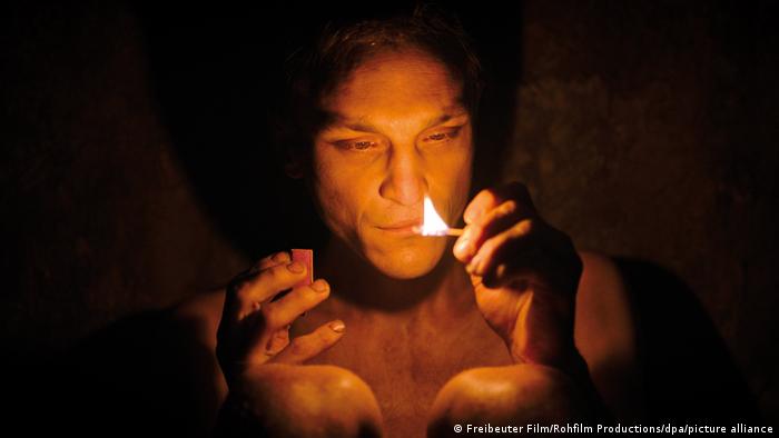 Naked man holds a lit match in his hand in the dark 