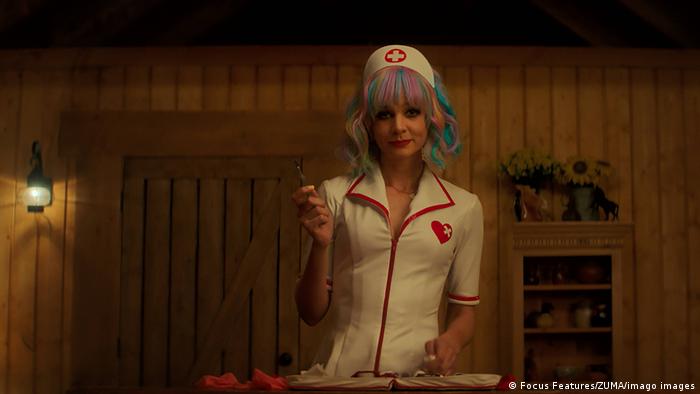 Still from 'Promising Young Woman' A woman dressed in a nurse's outfit and a colorful wig stands in a bedroom.