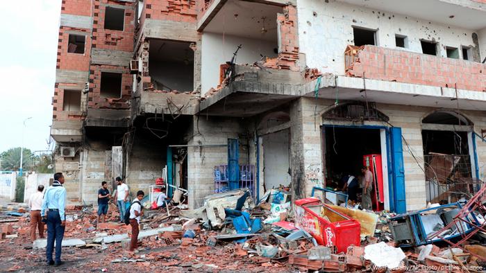 People stand amid debris at the site of a deadly car bomb attack close to a security checkpoint outside Aden’s international airport, in the neighborhood of Khormaksar, in the southern city of Aden, Yemen.