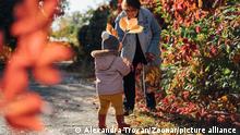 Granny and toddler baby collecting yellow leaves outdoors in a asunny autumn day