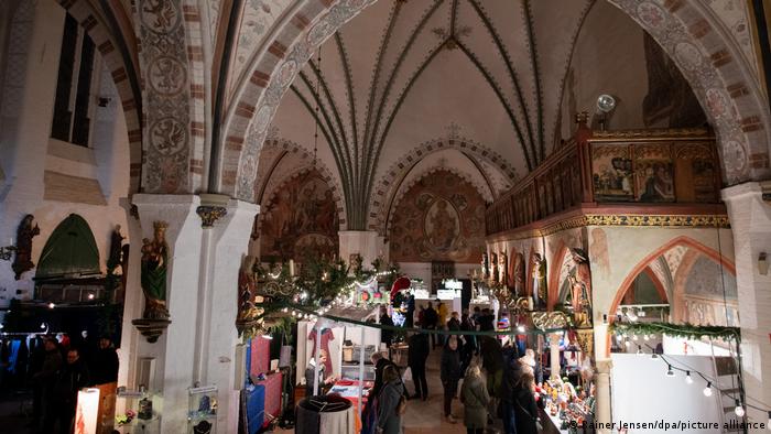 Orang-orang di pasar Natal dalam ruangan di bekas Rumah Sakit Roh Kudus Lübeck, Jerman