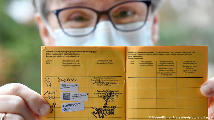 A person with smiling eyes and a face mask proudly presents vaccine documents showing a booster shot against COVID-19