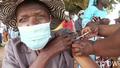 Elderly person wearing mask and hat being vaccinated outdoors in Kenya