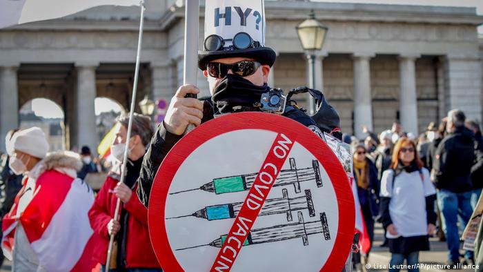 A masked man hold up a sign that reads 'No COVID vaccines'