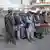 Homens afegãos aguardam atrás de cancela controlada por homem em trajes militares.