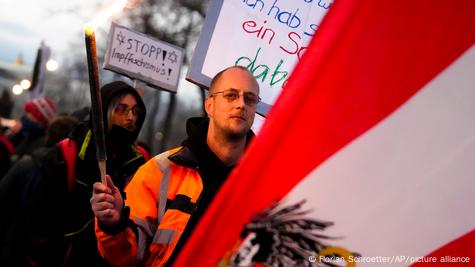 Manifestante segura tocha e outro carrega cartaz contra vacinação.