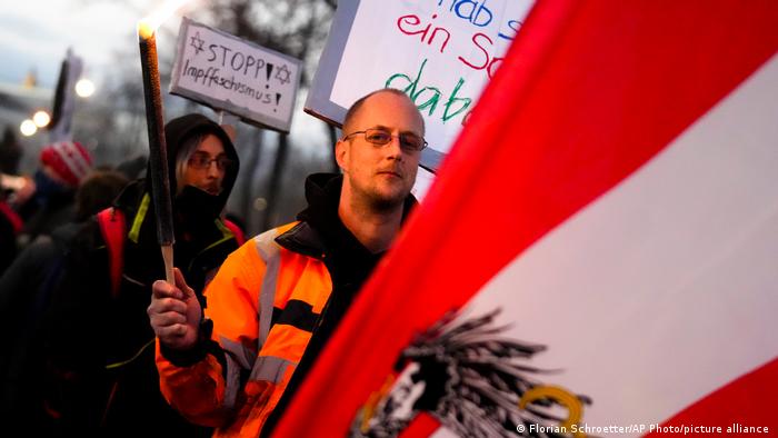 A protestor holds a flare as he walks behind an Austrian national flag 