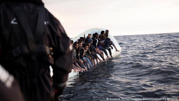 Eine Gruppe von Menschen sitzt am Rand eines Bootes, das im Meer kentert