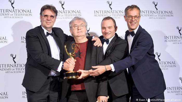 Michel Feller, Dominique Besnehard, Aurelien Larger and Harold Valentin stehen nebeneinander und lächeln in die Kamera, in der Hand halten sie die Trophäe der Internationale Emmy Awards