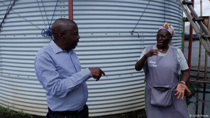 Entrepreneur Jack Kahorha in front of a water reservoir with Eugenie Fatuma Anyenyeri, who manages the tank