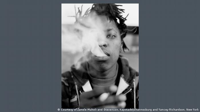 Photograph by Zanele Muholi showing a person blowing cigarette smoke in the direction of the camera lens