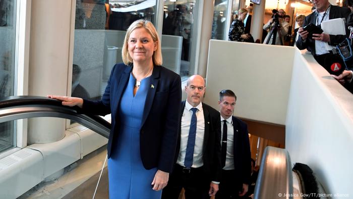 Magdalena Andersson standing in front of two men on an escalator